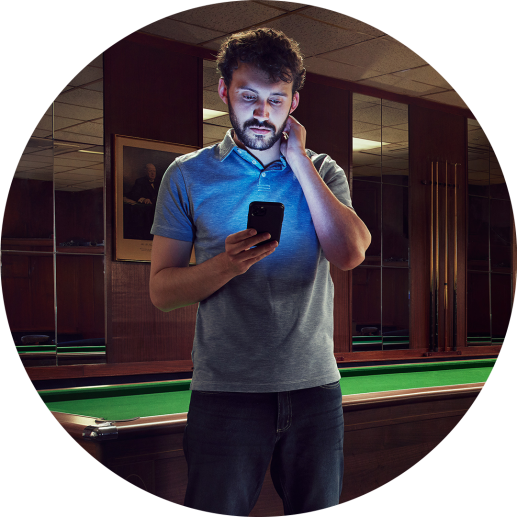 Man stood in front of a snooker table looking at his phone, seeming unsure as to whether or not he should reach out